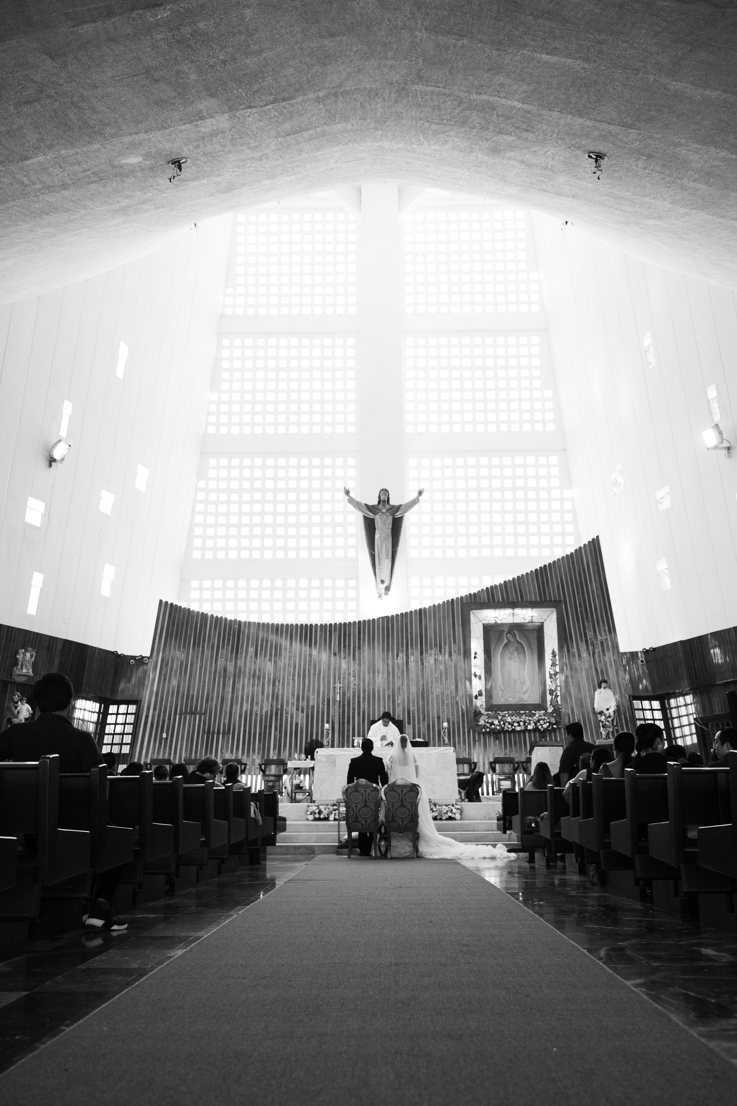 Black and white interior of a church with pews, altar, and a statue of Jesus Christ above the sanctuary.