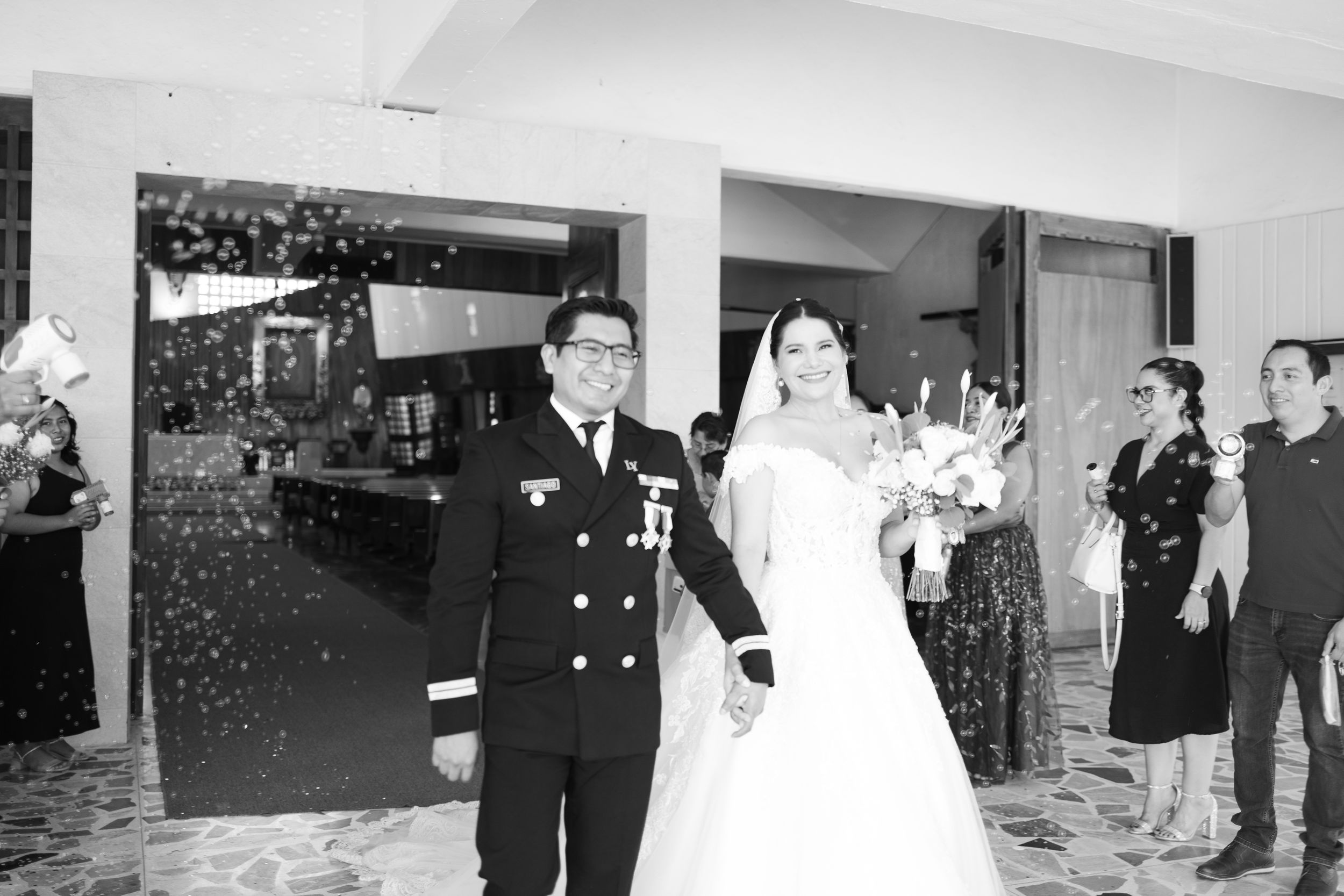 Black and white photo of a military groom and bride in wedding dress walking out to confetti celebration.