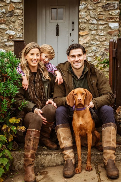 Smiling family with young child and Vizsla dog sitting on cottage doorstep in autumn.