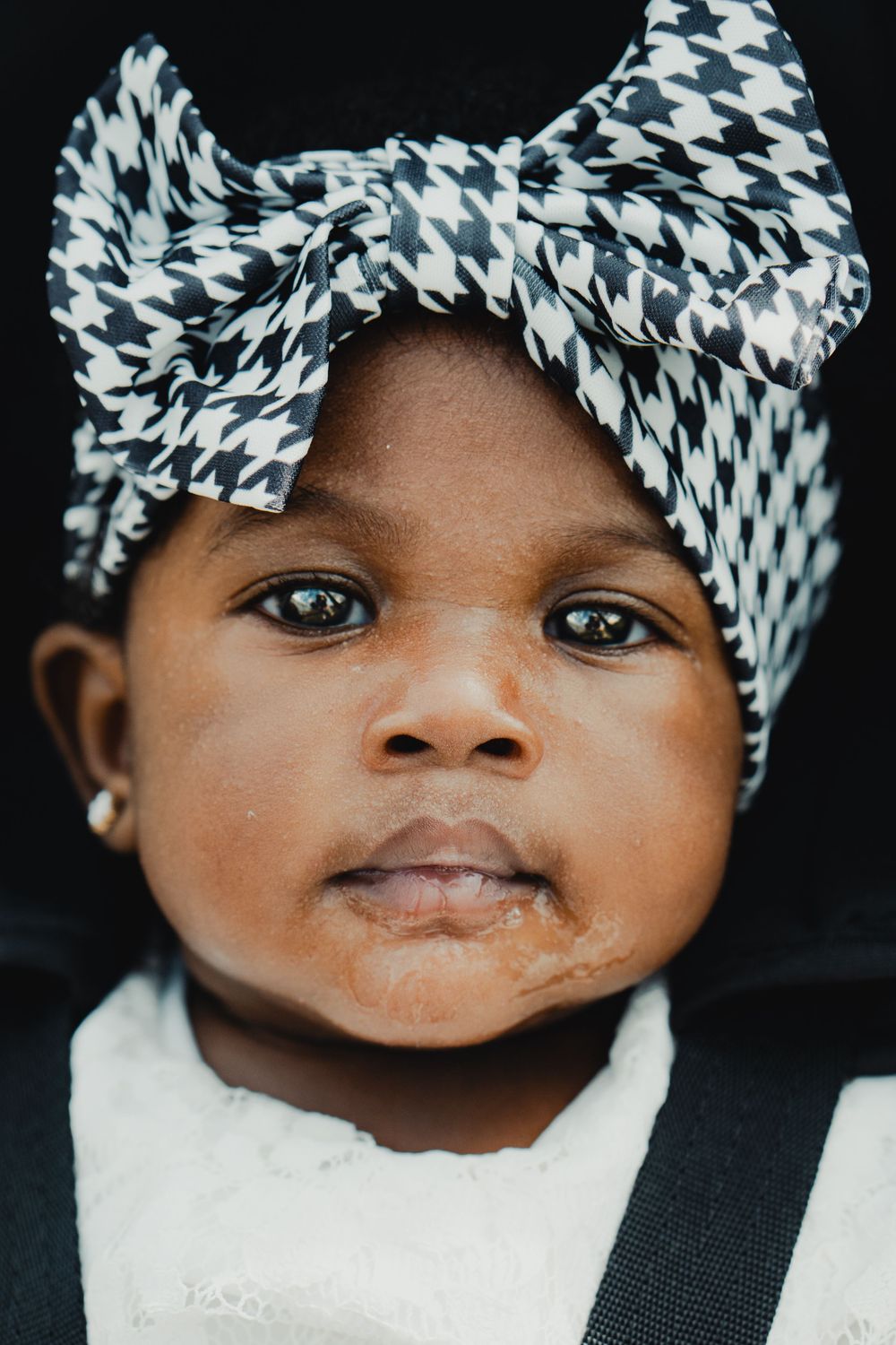 Adorable baby girl wearing a black and white houndstooth bow headband with small stud earrings.