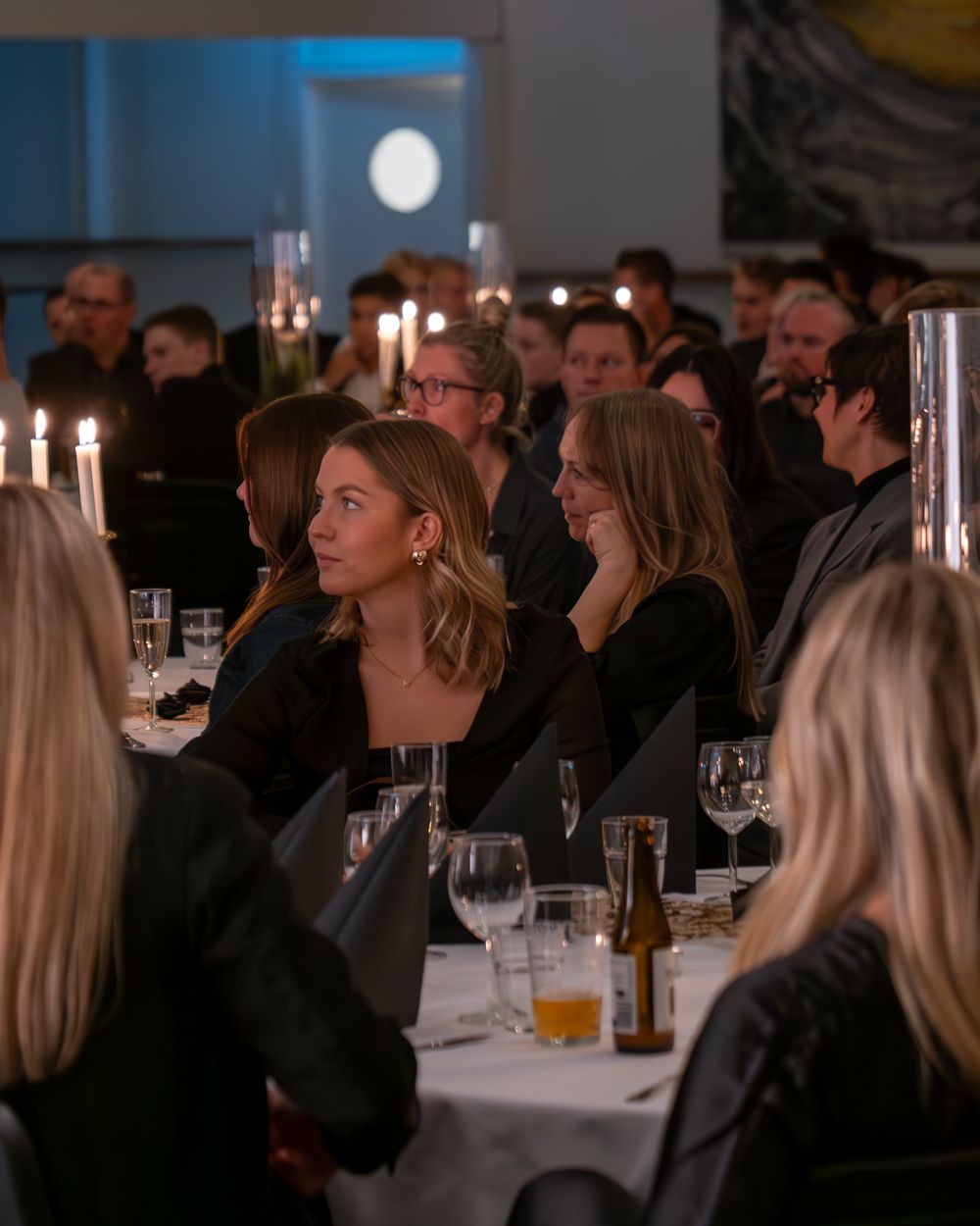 Sittande personer vid bord under ett event. Alla är vridna mot och lyssnar på den som pratar på scenen.