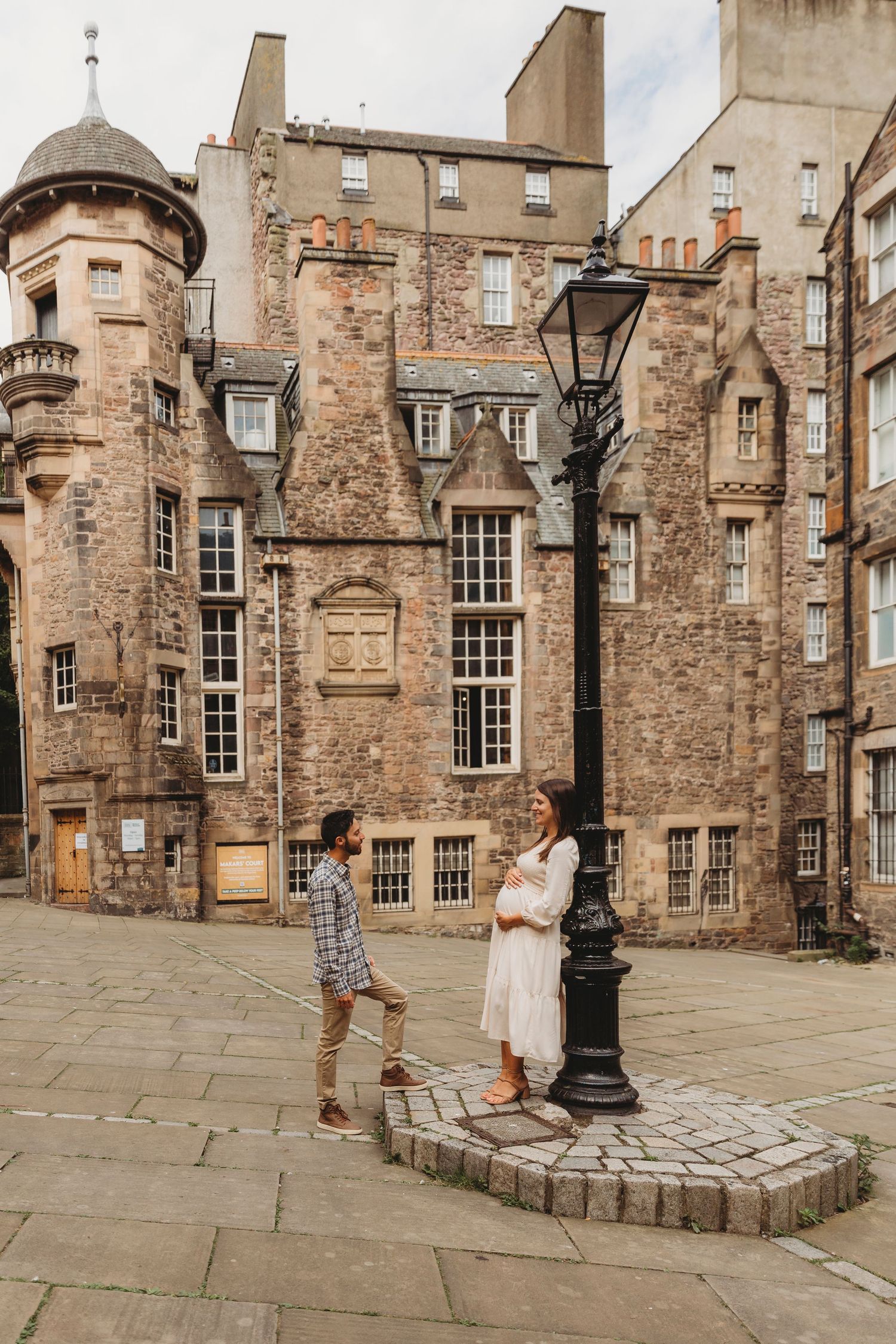 Couple standing by a vintage lamppost in a historic Edinburgh stone courtyard with Gothic architecture.