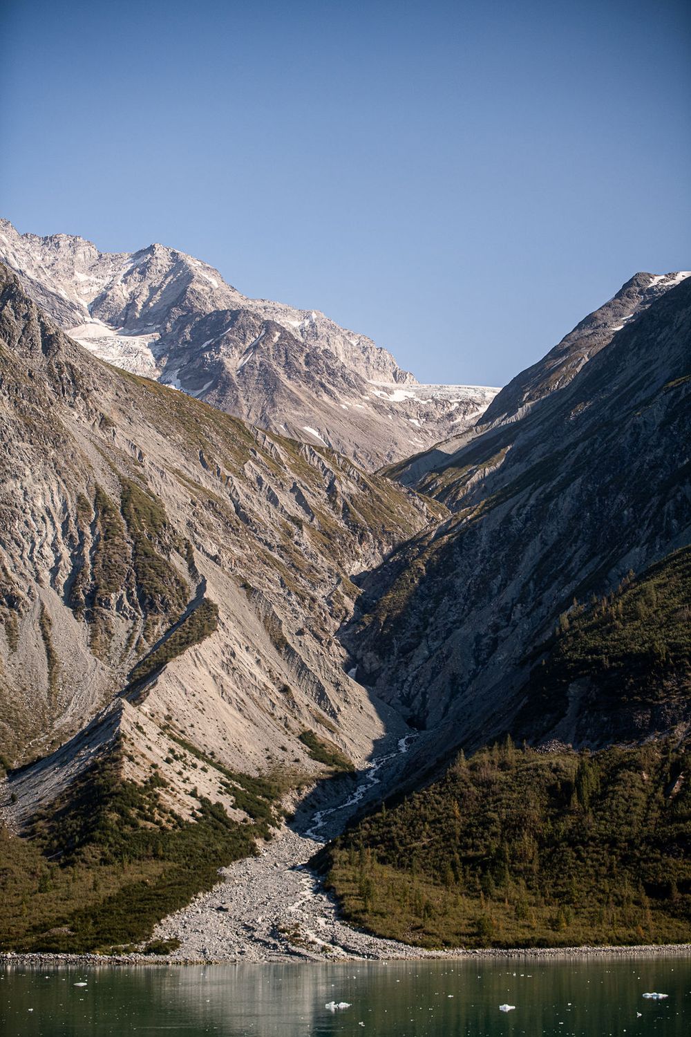 Dramatic glacial valley with rocky snow-capped peaks descending to a turquoise bay with floating ice.