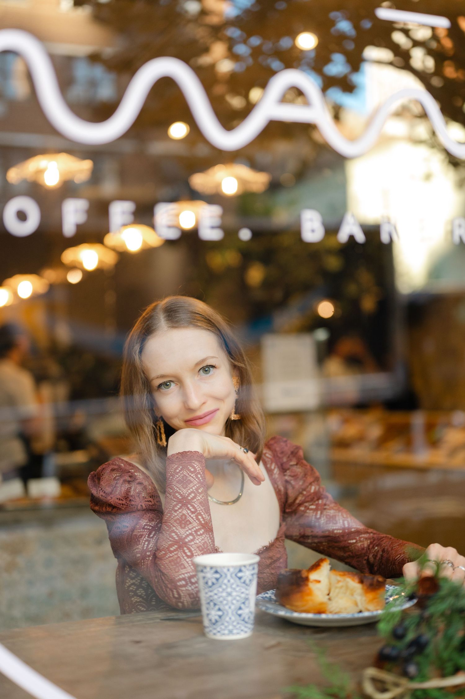 Young woman smiling at a coffee bar, sitting by window with a cup and pastry on the Upper East Side, NYC during a personal branding session.