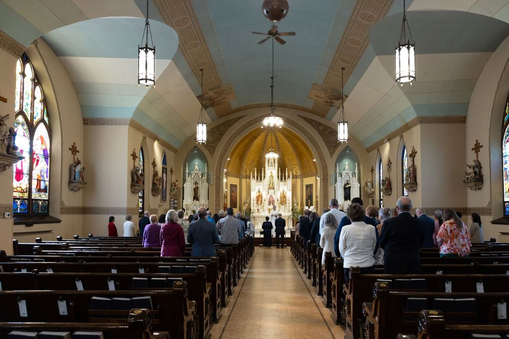 Guests standing in pews during a Catholic church wedding ceremony with ornate stained glass windows.