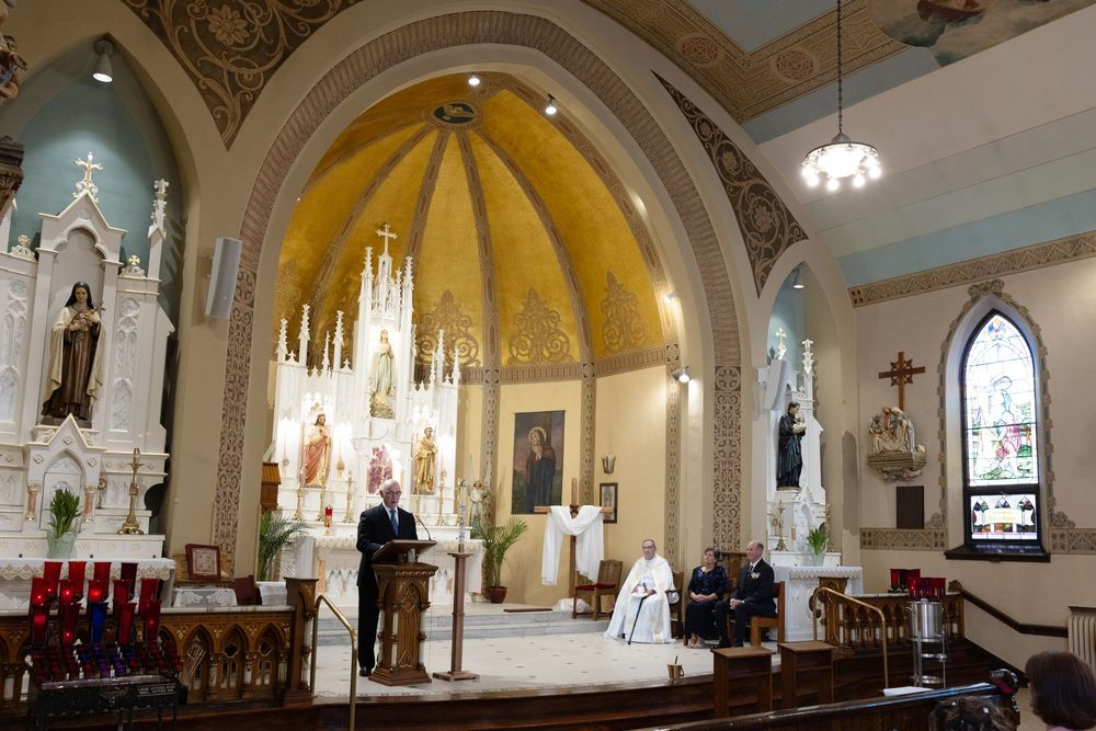 Catholic church interior with ornate altar, golden dome, and congregation during a formal religious ceremony.