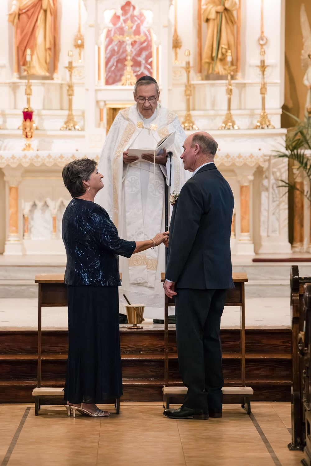 Couple exchanging vows before a priest at a Catholic church altar during a wedding ceremony.