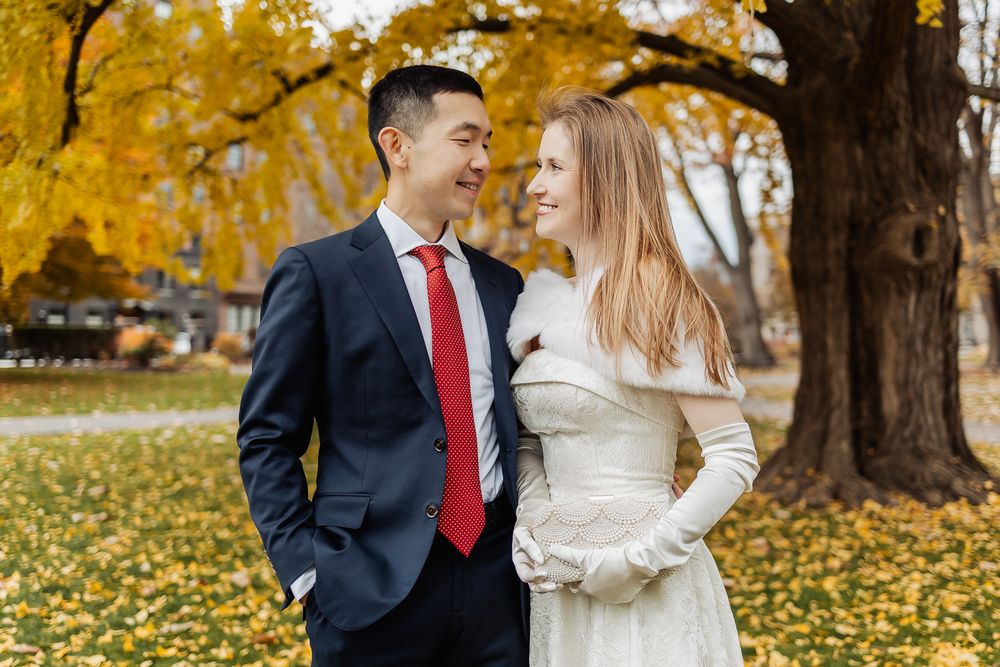 Newlyweds sharing a romantic glance outdoors, groom in navy suit, bride in elegant white dress, fall foliage.