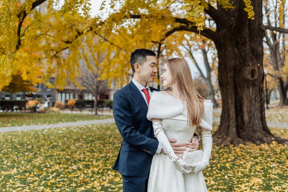 Interracial wedding couple sharing a tender moment under vibrant yellow autumn trees in a scenic park setting.
