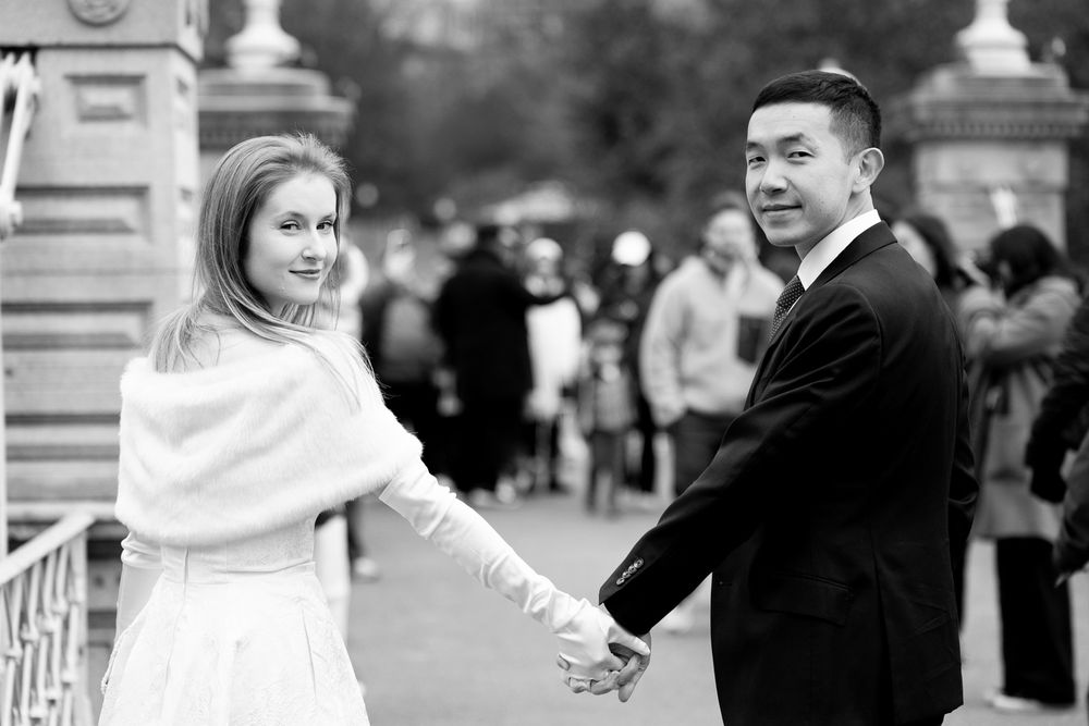 Bride and groom holding hands in black and white wedding photo outdoors.