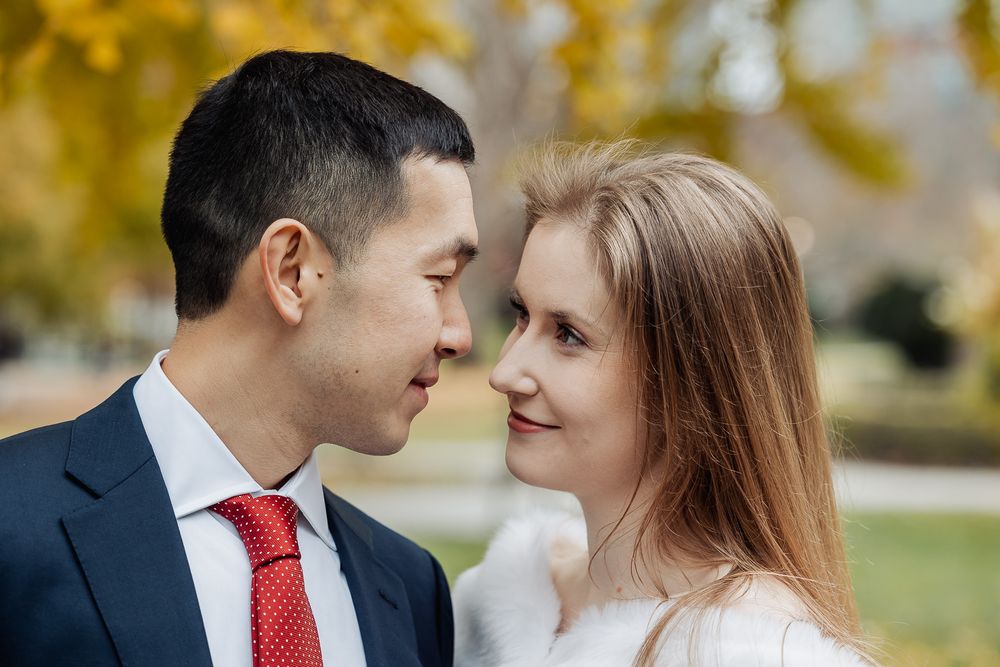 Couple in wedding attire gazing into each other's eyes outdoors with autumn foliage backdrop.