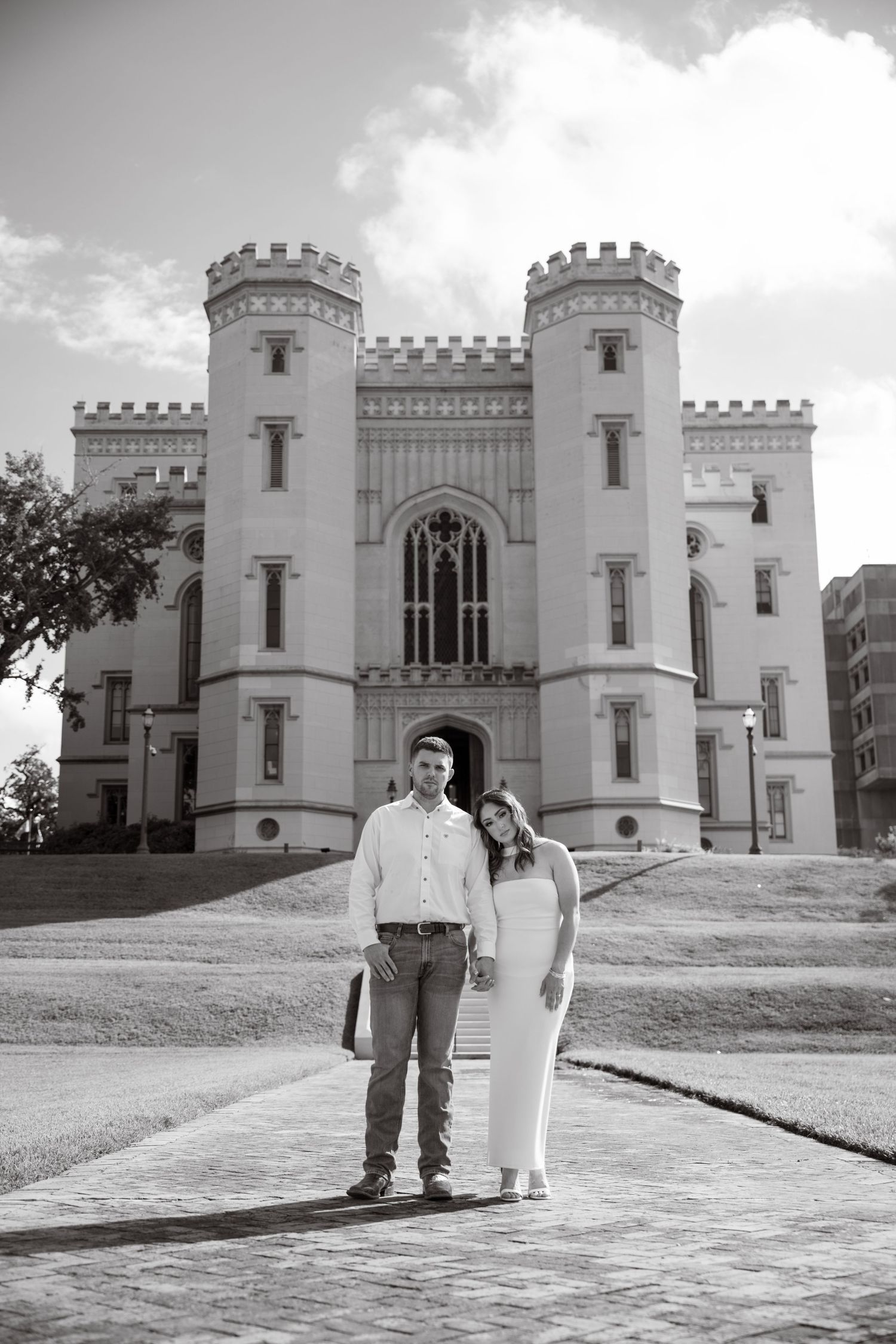 Black and white beach wedding photo of bride in lace gown and groom in suit embracing, hair blowing in wind.