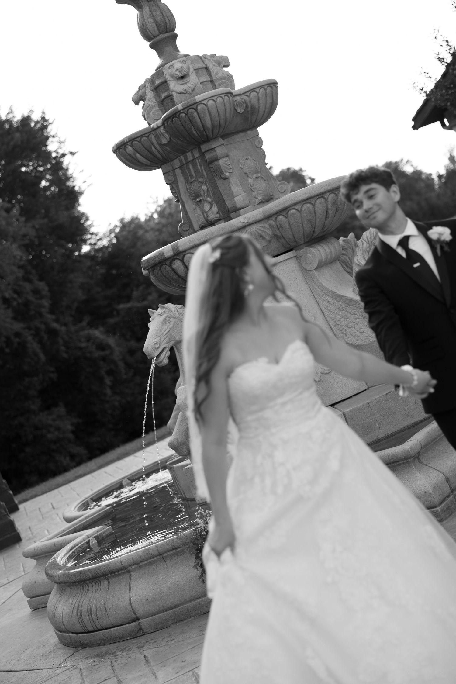 Bride and groom share a romantic moment by an ornate stone fountain in black and white.
