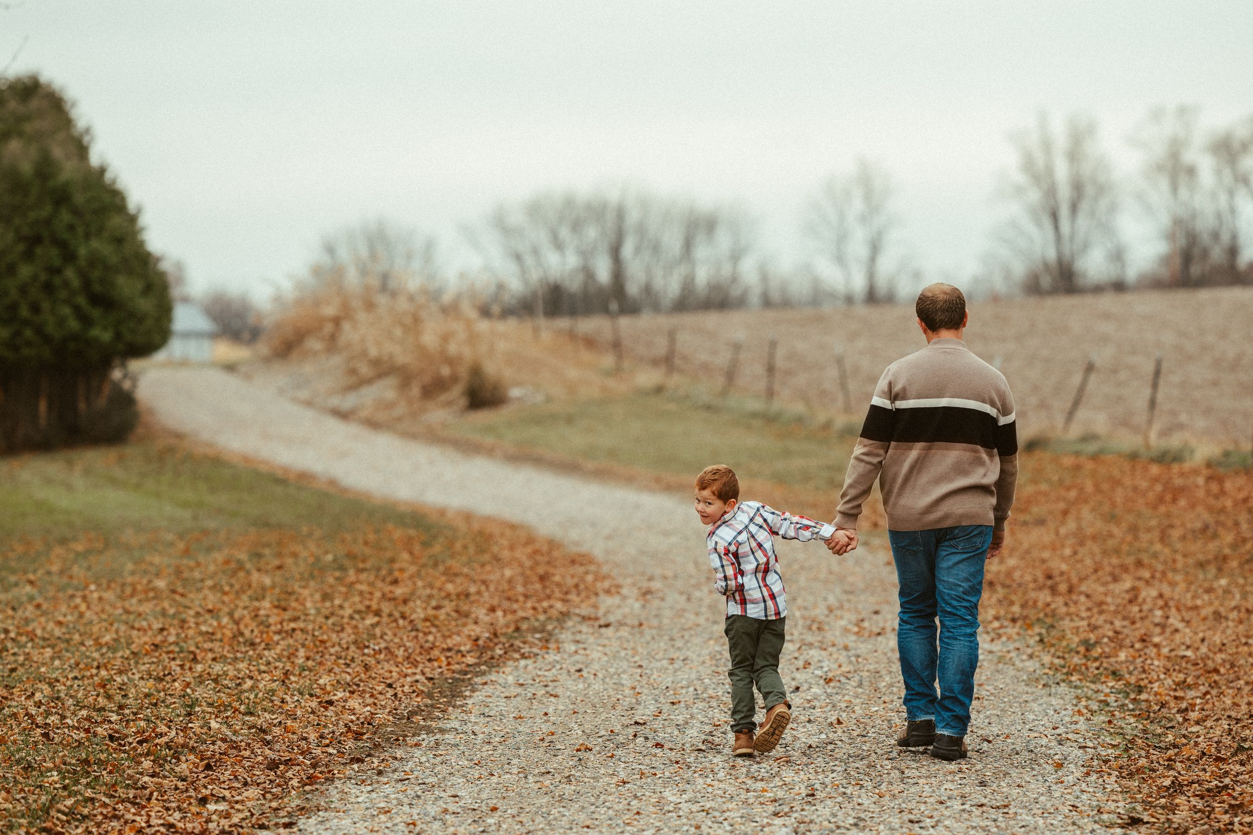 Father and young son walking hand in hand down a rural gravel path in autumn.