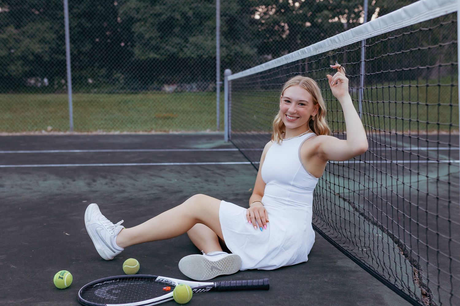 High school senior smiling during a senior photography session with tennis gear to showcase their love for the sport