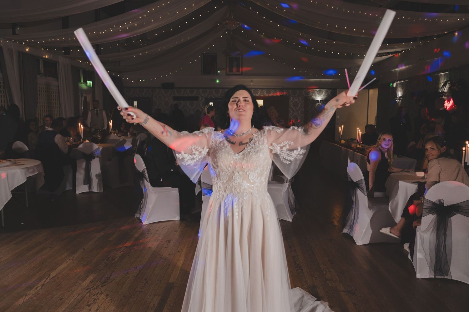 A group of dancers in white dresses perform synchronized movements on a dark dance floor during a celebration.