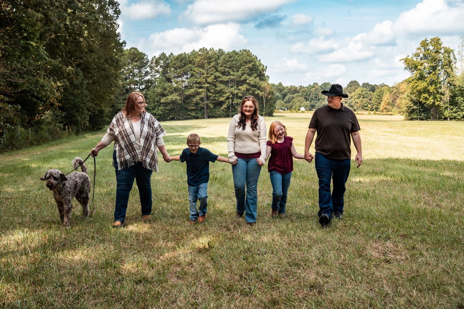 A group of people stand together in a grassy field on a sunny day with trees in the background.