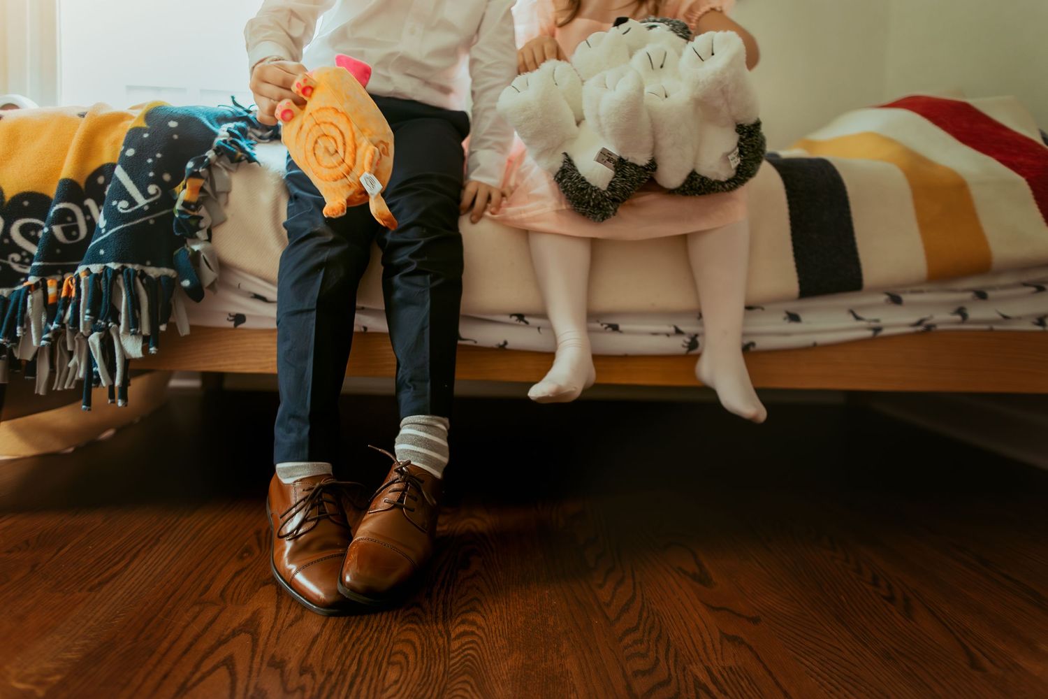 Close-up view of feet wearing brown leather boots on a wooden floor with plush toys visible in the background.