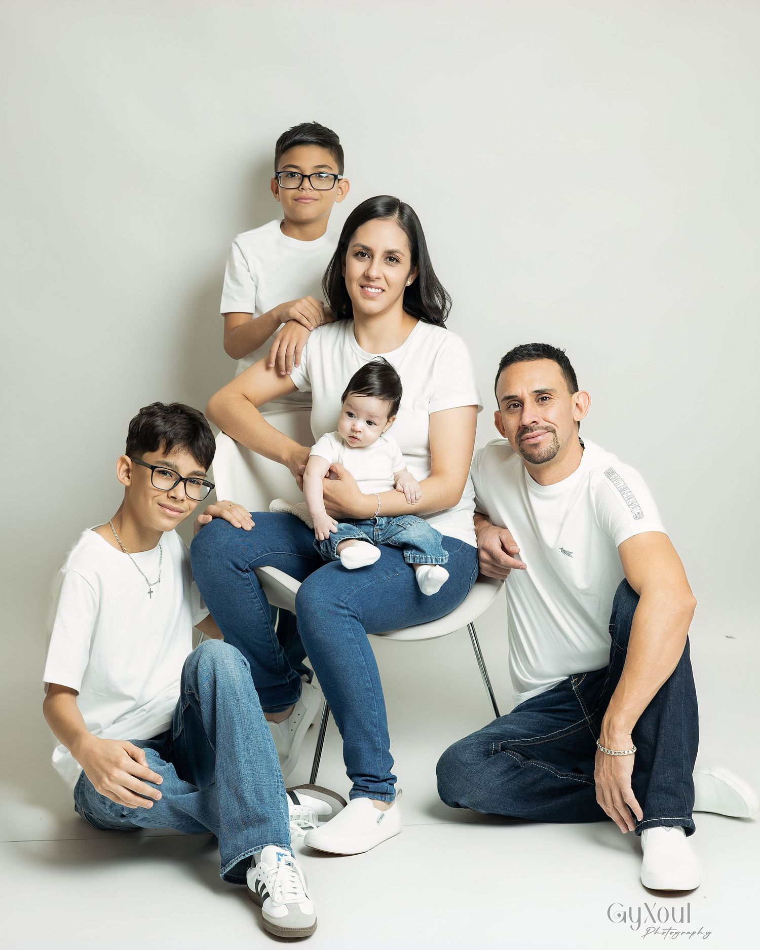 Family portrait session showing casual poses on white background in matching white shirts and blue jeans.