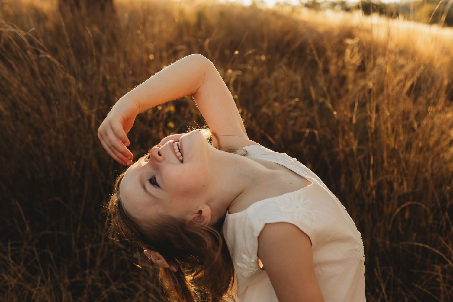 A joyful figure in a white top leans back in a golden wheat field at sunset, creating a dreamy outdoor portrait.