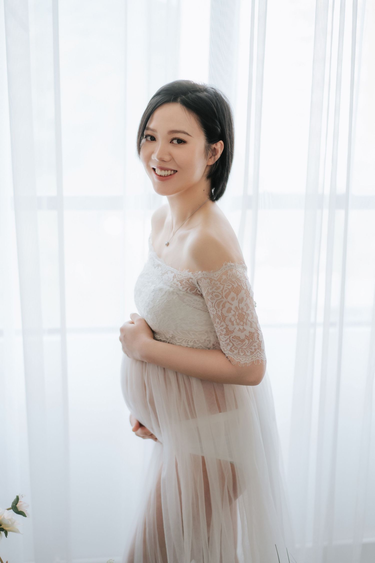A baby in a floral dress smiles while sitting against a white backdrop with balloons.