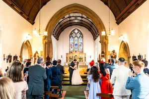Wedding ceremony inside a traditional English church with guests seated in wooden pews.