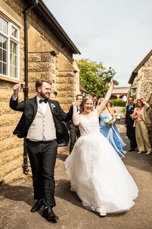 Ecstatic newlyweds celebrate outside church as wedding guests cheer during confetti exit.