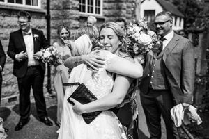 Bride in lace wedding dress shares warm embrace with wedding guest after ceremony.
