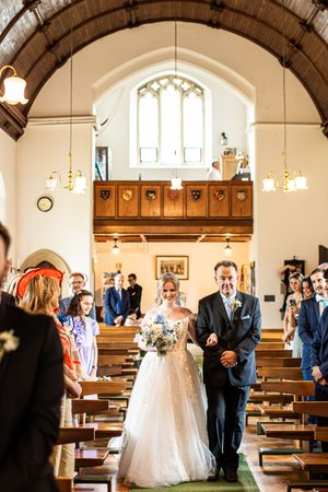 Bride walks down church aisle with father during traditional wedding ceremony.