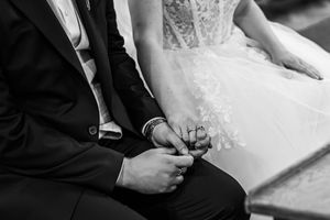 Close-up black and white photo of bride and groom holding hands during wedding ceremony.