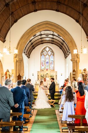 Wide angle view of bride and groom at church altar during wedding ceremony with guests seated.