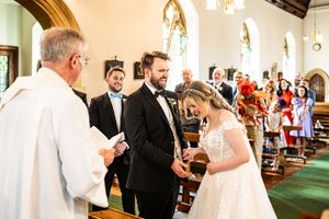 Bride and groom exchange rings before officiant during traditional church wedding ceremony.