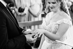 Bride placing wedding ring on groom's finger during church ceremony in black and white photography.