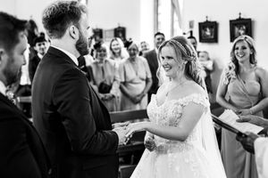 Smiling bride and groom exchange vows before wedding guests inside a church ceremony.