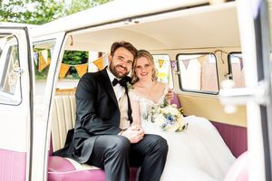 Bride and groom smiling inside a vintage VW camper van decorated with bunting on their wedding day.