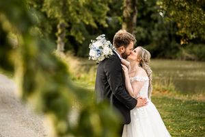 Bride and groom sharing a romantic kiss near a pond surrounded by lush greenery.