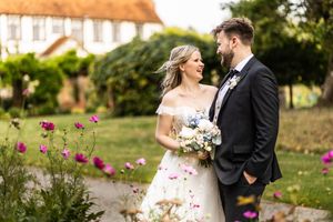Bride and groom smiling at each other in a colorful flower garden on their wedding day.