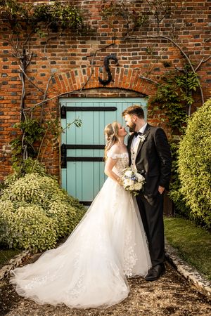 Bride and groom kissing in front of a charming teal wooden door set in a brick arch.
