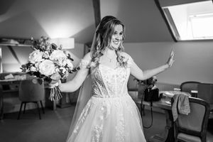 Black and white photo of bride in lace gown laughing while holding bouquet in bridal suite.