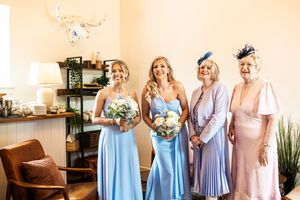 Bride with two bridesmaids in blue gowns and two older guests pose together smiling indoors.