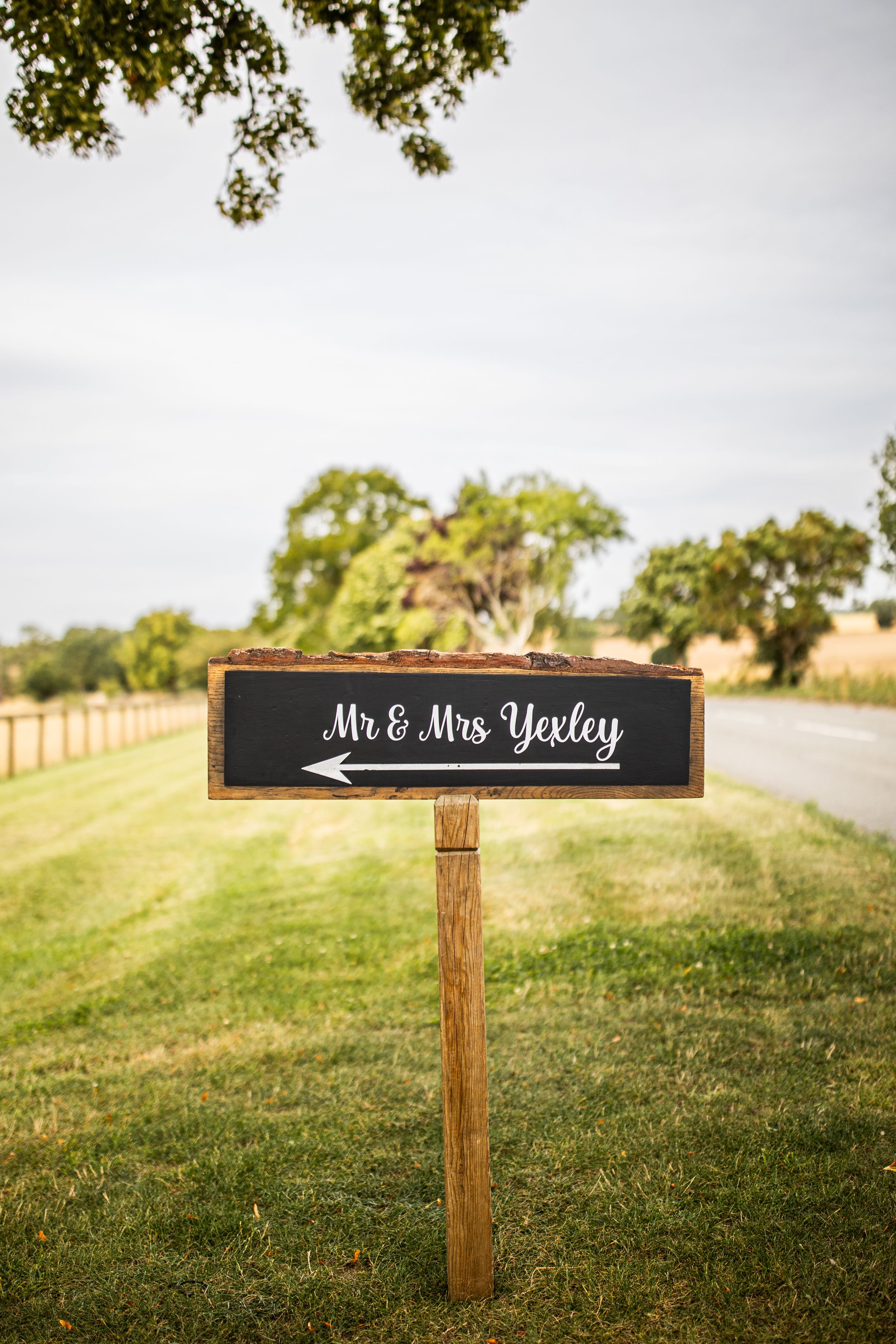 Rustic chalkboard sign directing guests to Mr and Mrs Yexley wedding venue on grassy lawn.
