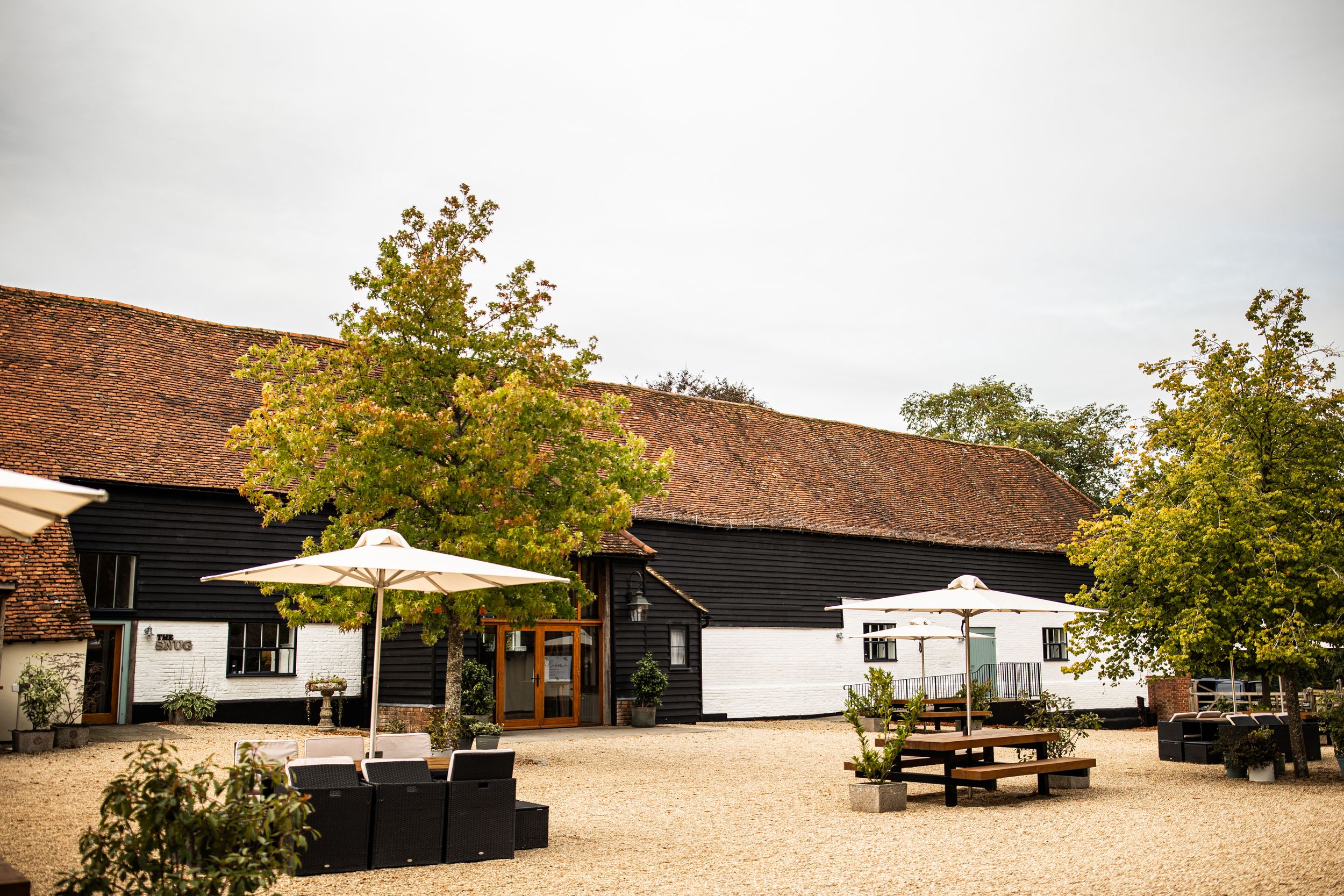 Charming rustic barn wedding venue with outdoor seating and umbrellas on a cloudy day.