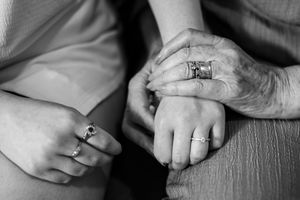 Close-up black and white photo of three generations of women holding hands, wearing elegant rings at a wedding.