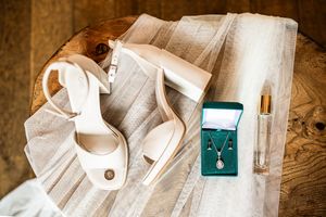Bridal accessories flat lay featuring nude heels, veil, diamond jewelry in green box, and perfume.