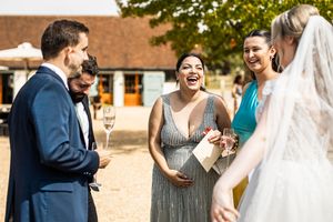 Bride and wedding guests laughing together outdoors at a sunny barn wedding reception.