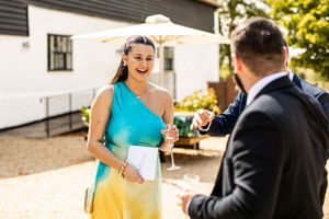 Smiling wedding guest in a colorful one-shoulder dress chatting with a suited guest outdoors.