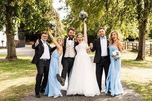 Bride and groom celebrating with bridesmaids and groomsmen in light blue attire outdoors.