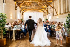 Bride and groom entering a rustic barn wedding reception hall filled with seated guests.