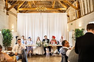 Wedding party at rustic barn venue head table during reception speeches with exposed timber roof.