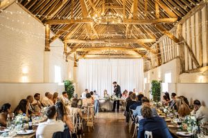 Wide angle view of elegant barn wedding reception with guests seated at long dining tables.